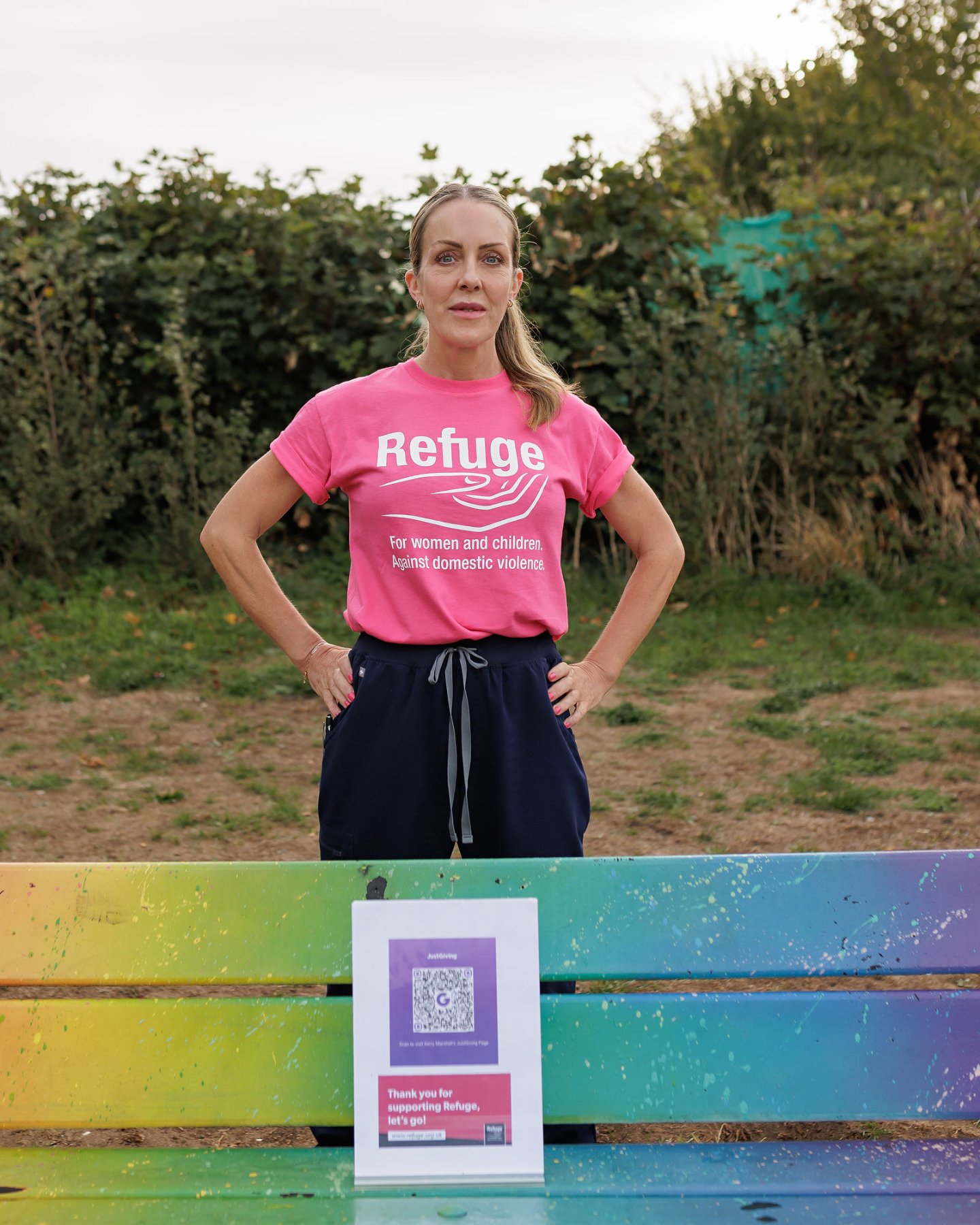 Kerry Marshall Shergold in a pink Refuge T-shirt behind a rainbow bench with the JustGiving QR code