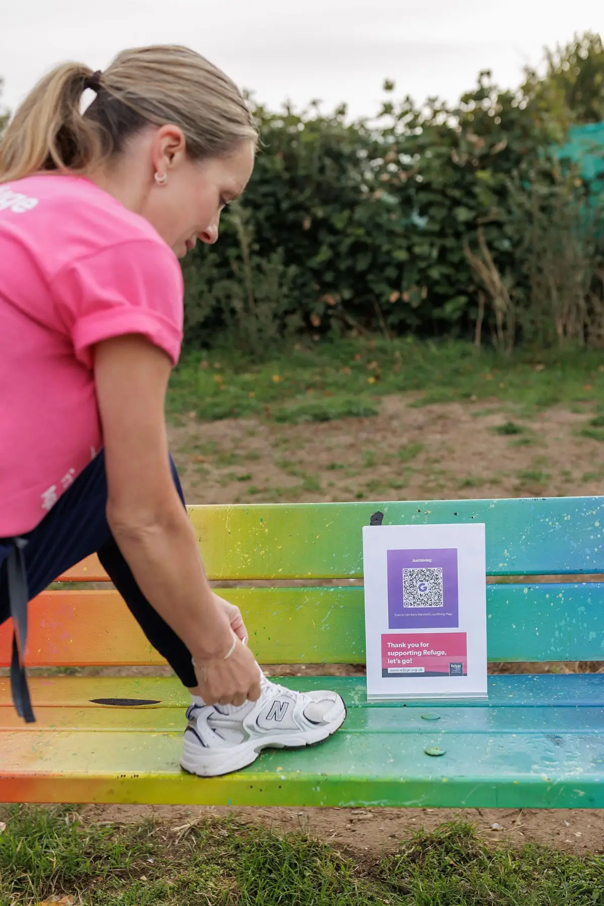 Kerry lacing her trainers on a rainbow bench beside the Refuge JustGiving QR code